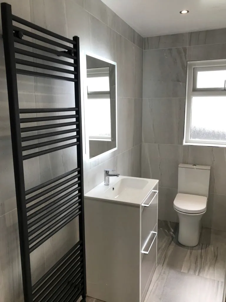 Tall black heated towel rail beside an LED mirror